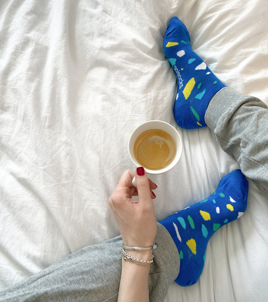 Goisocks csodás kék kavicsos bokazokni egy lány lábain, kávéval a kezében.