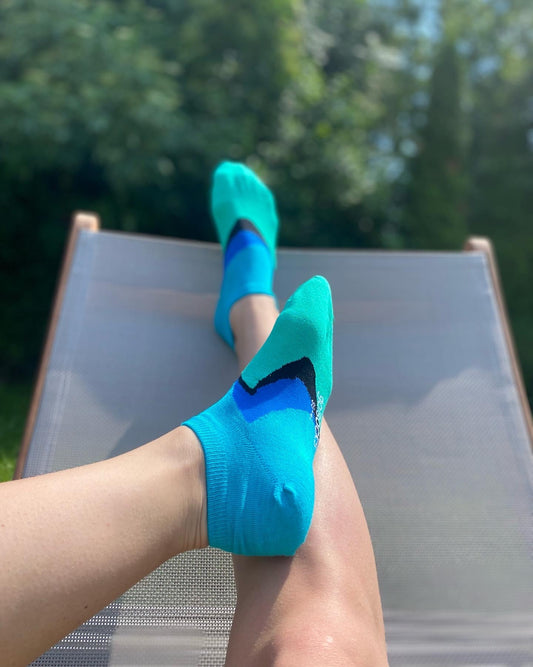 Egy lány a kertben lábain Goisocks bokazoknit visel, kék, zöld és fekete hullámos mintával.